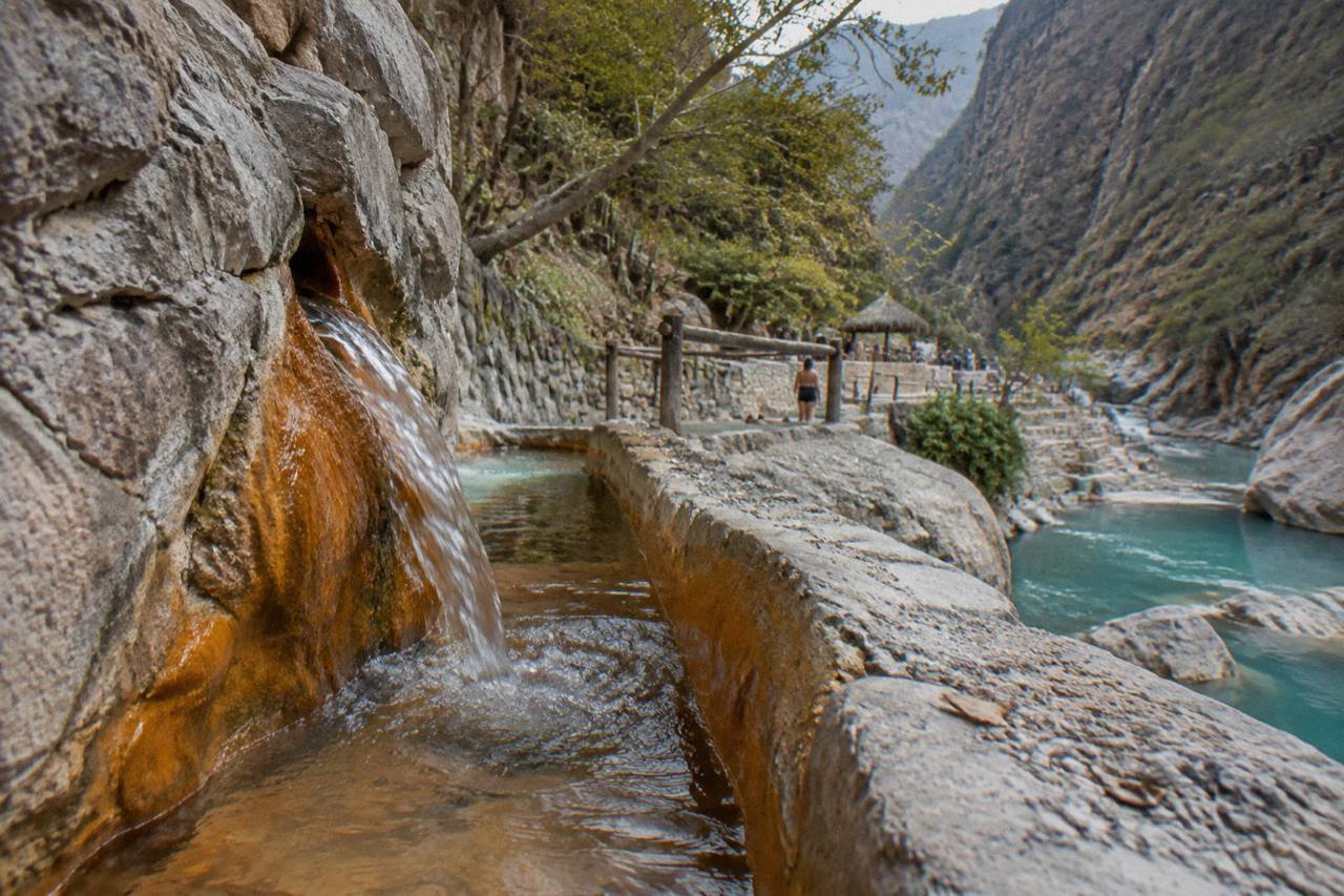 Warm spring water flowing from rock into a stone-lined channel inside a canyon