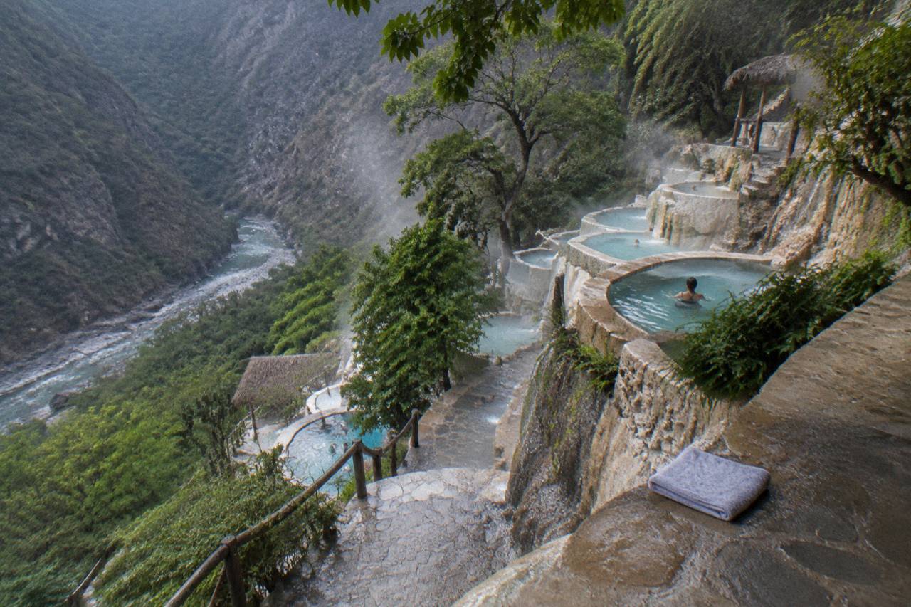 Rows of small terraced thermal pools built along a steep green canyon slope