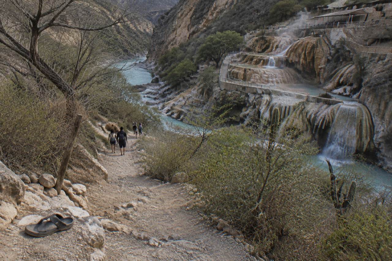 A tour group walking a canyon trail toward steaming turquoise water below