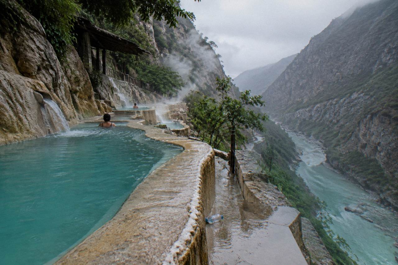 Steaming thermal pools built into a steep canyon wall above a turquoise river