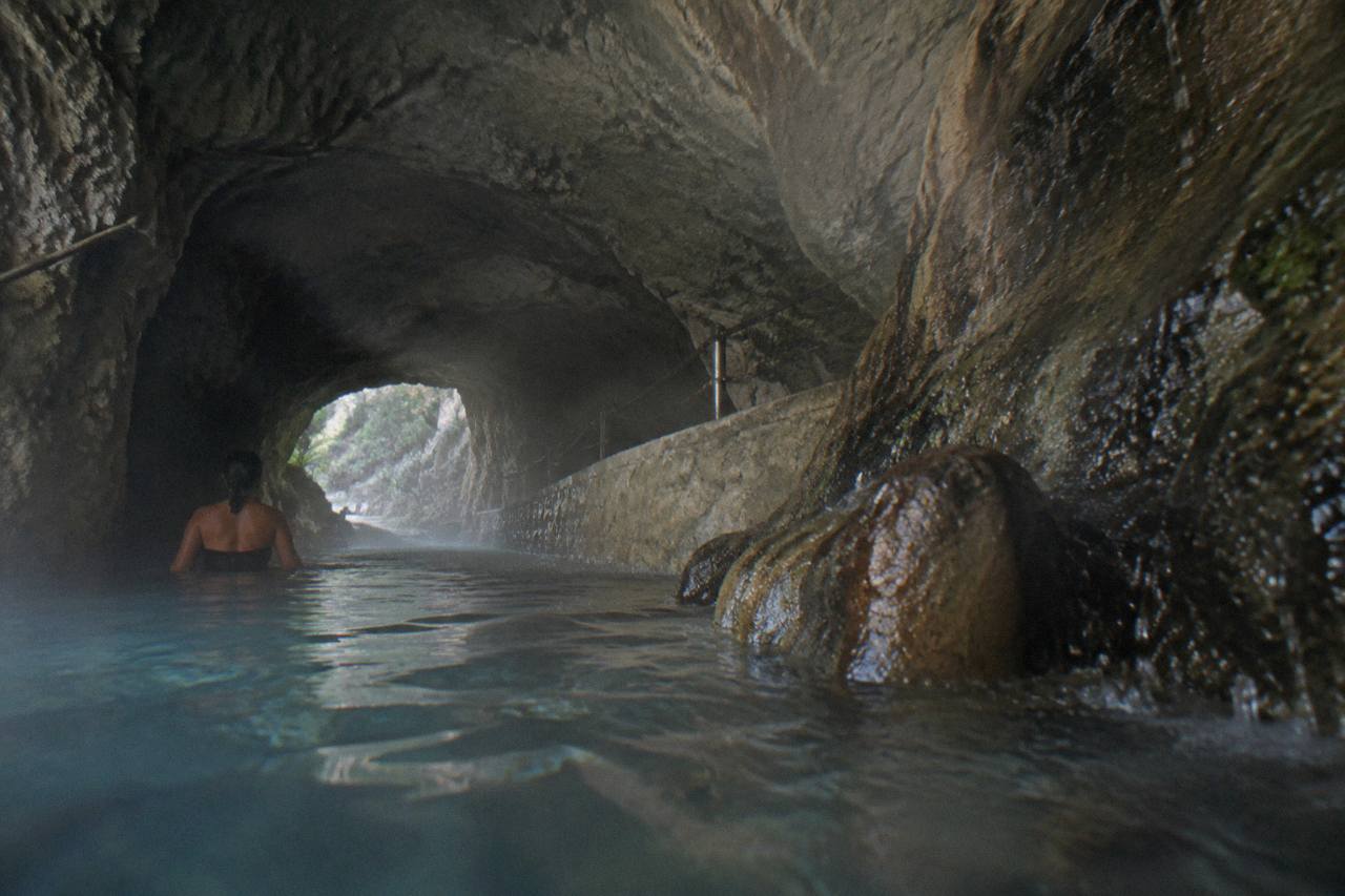 Warm water and steam inside a dim rock tunnel with rough stone walls