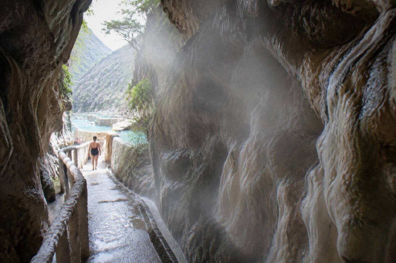 A narrow steamy passage between rock walls lit by daylight at the far end