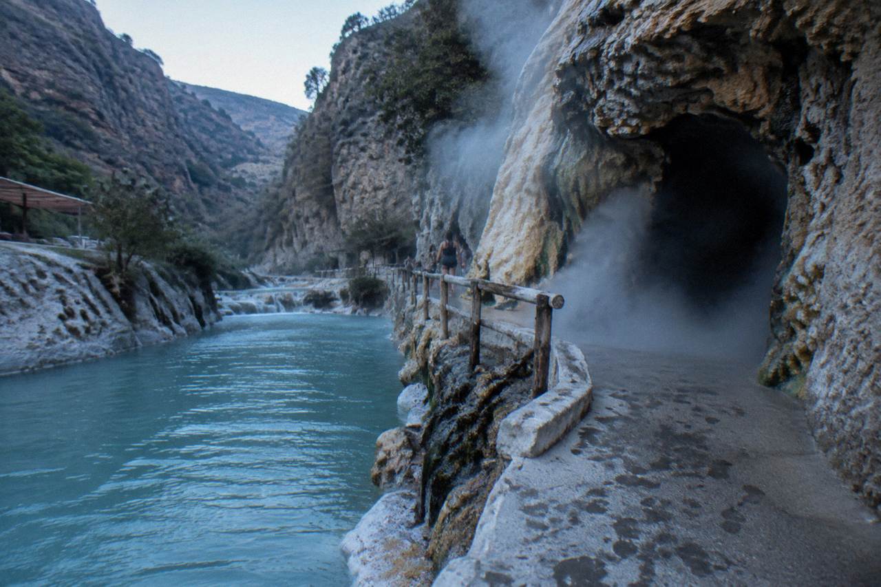 Steam rising from a rock tunnel opening onto a canyon wall above a turquoise river