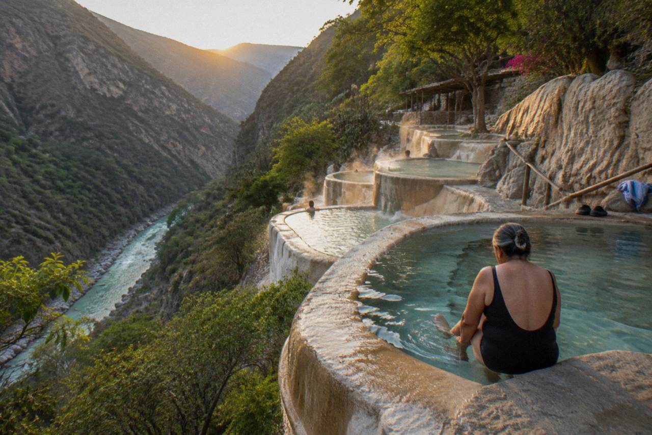 Terraced stone pools of steaming water descending a green canyon wall