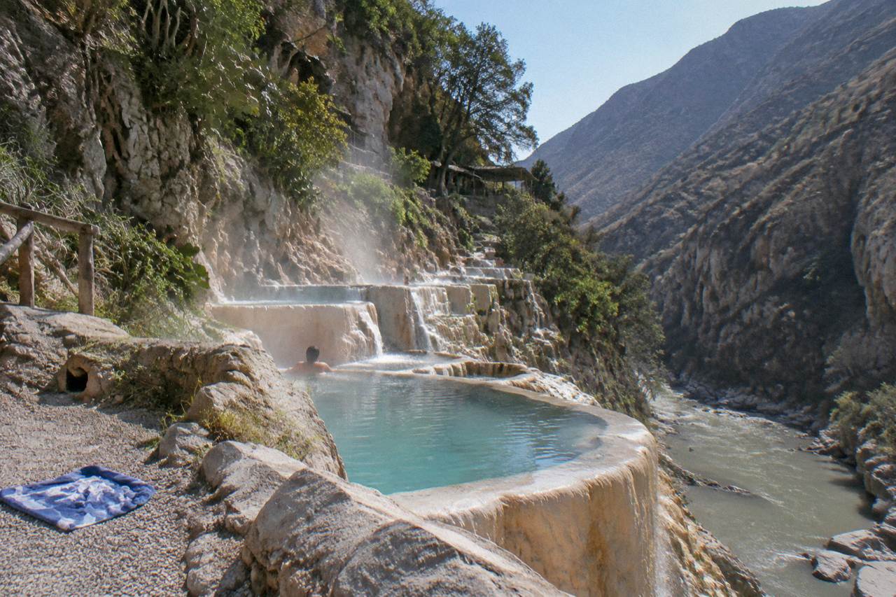 Steaming turquoise thermal pools built into a canyon wall above a warm river