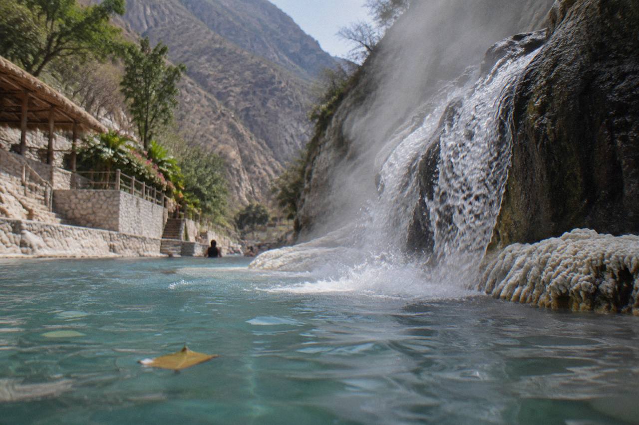 Steaming waterfall of thermal water spilling over rock into a canyon pool