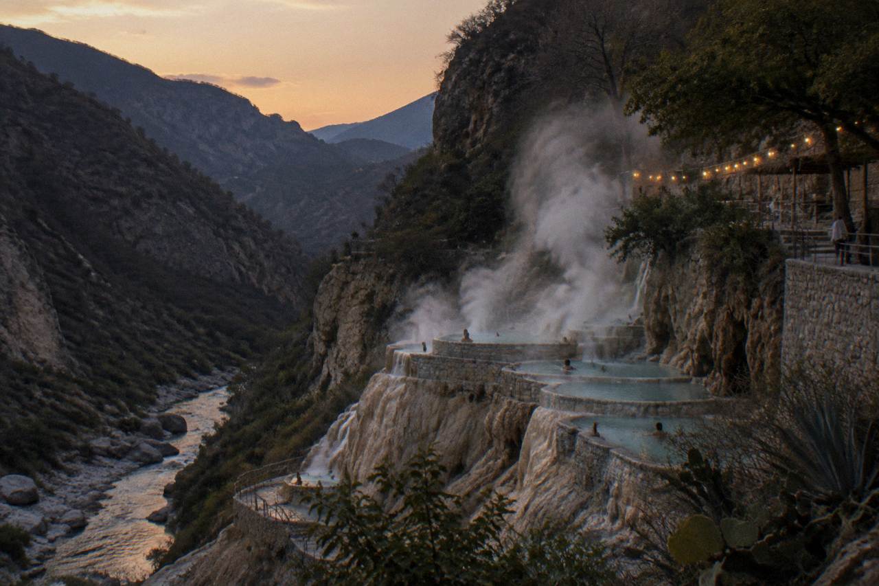 Steam rising from turquoise thermal pools built into a canyon wall