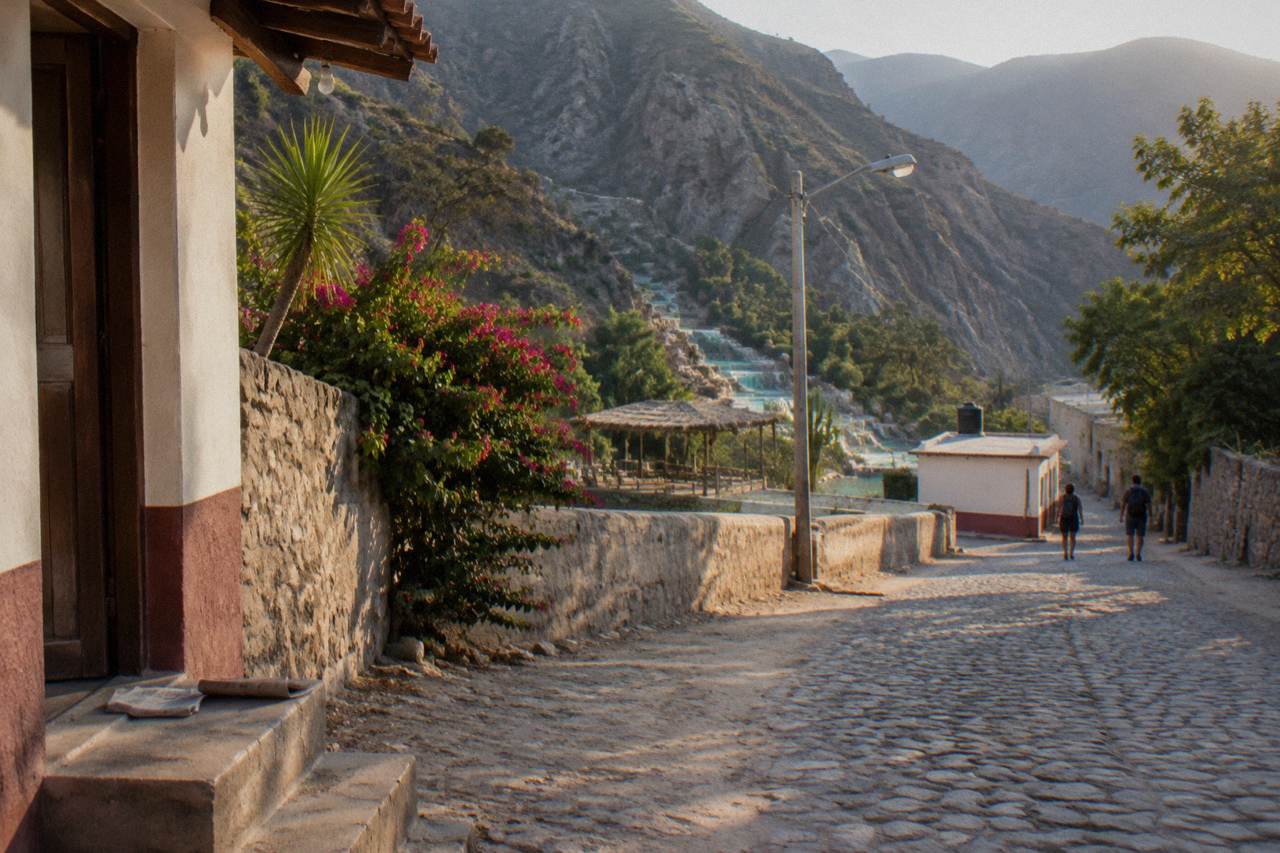 Quiet street in an inland Hidalgo town with parked cars and hills behind.