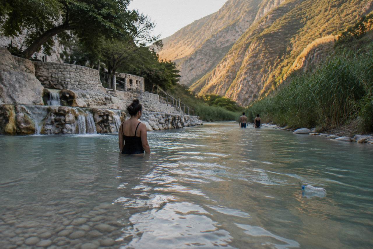 A calm turquoise thermal river flowing between tall green canyon walls in late afternoon light