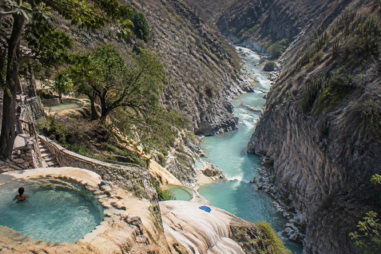 Steep canyon walls rising above a turquoise thermal river winding through the Tolantongo gorge