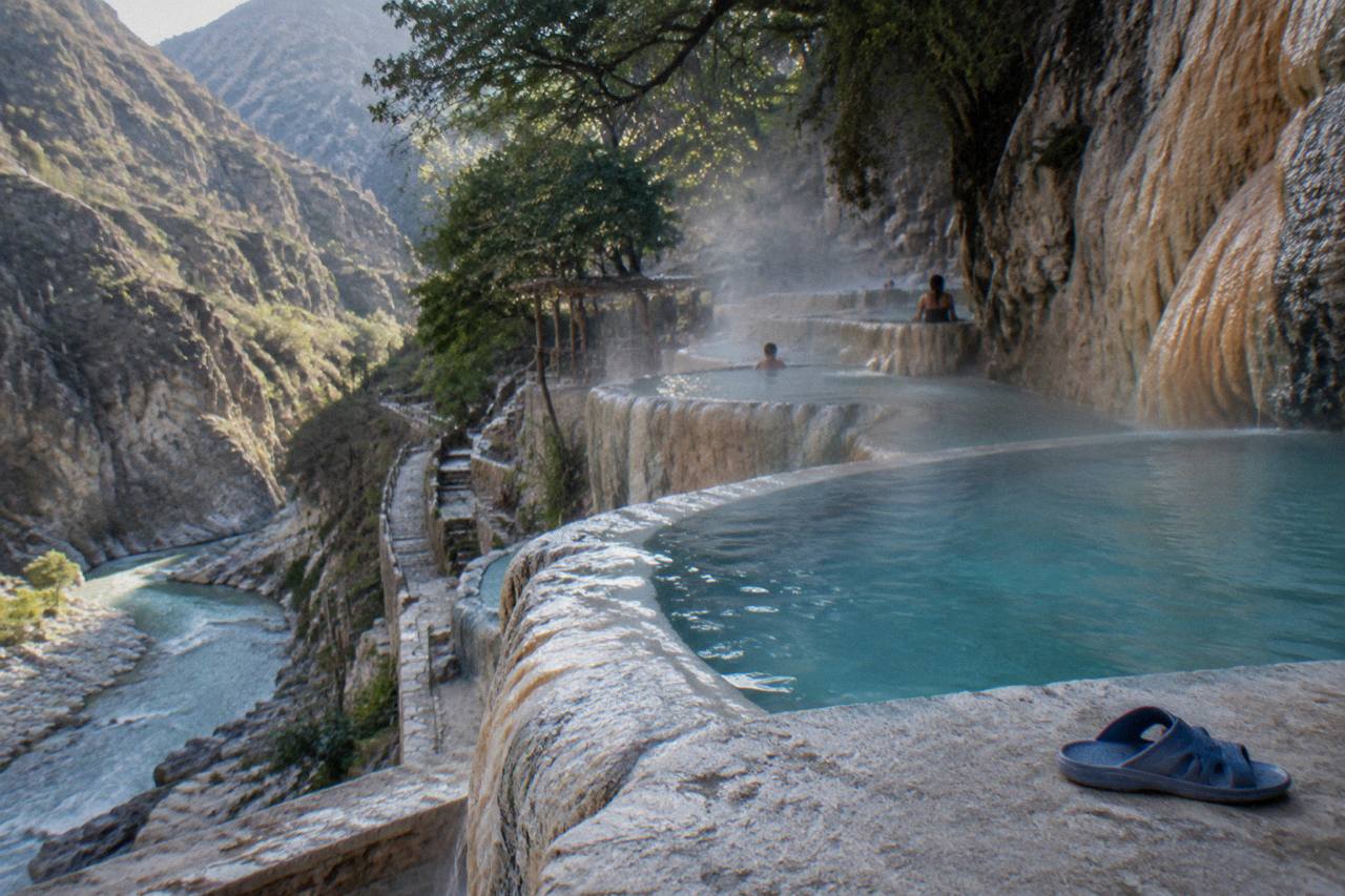 Canyon cliffs in morning light with steam rising from thermal pools along the riverbank