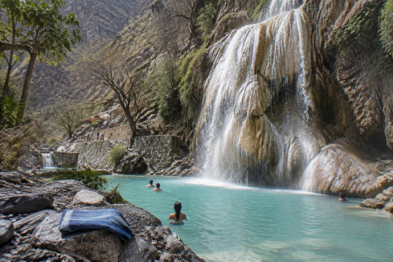 Waterfall dropping into a turquoise thermal pool between canyon walls
