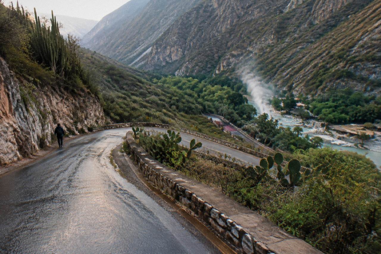 Mountain road winding down toward the green canyon holding the thermal pools of Grutas de Tolantongo
