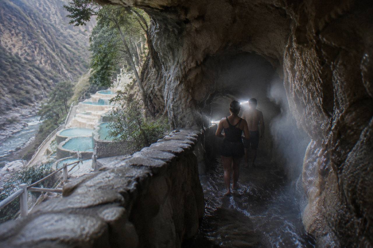 Steam-filled cave tunnel at Grutas de Tolantongo with thermal water flowing over the rock floor and visitors walking with headlamps