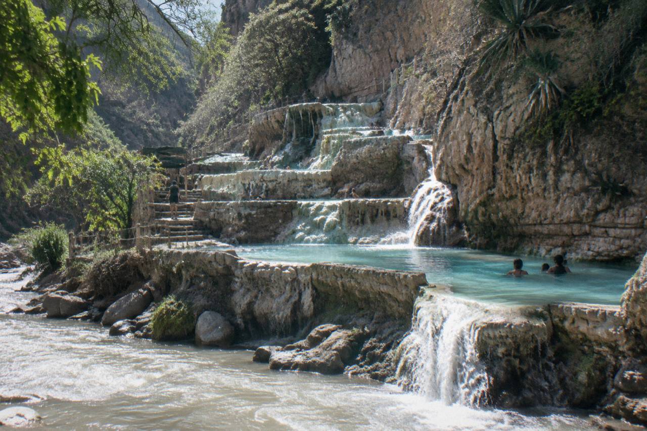 Terraced turquoise pools cascading down a canyon wall at Grutas de Tolantongo with the thermal river in the foreground
