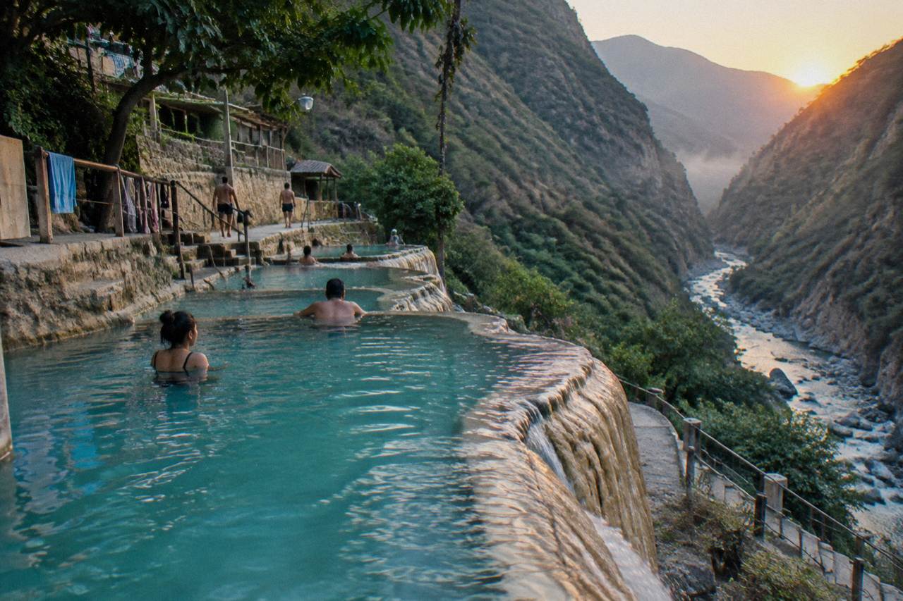 Turquoise thermal river cascading over travertine terraces at Grutas de Tolantongo, surrounded by canyon walls and lush greenery