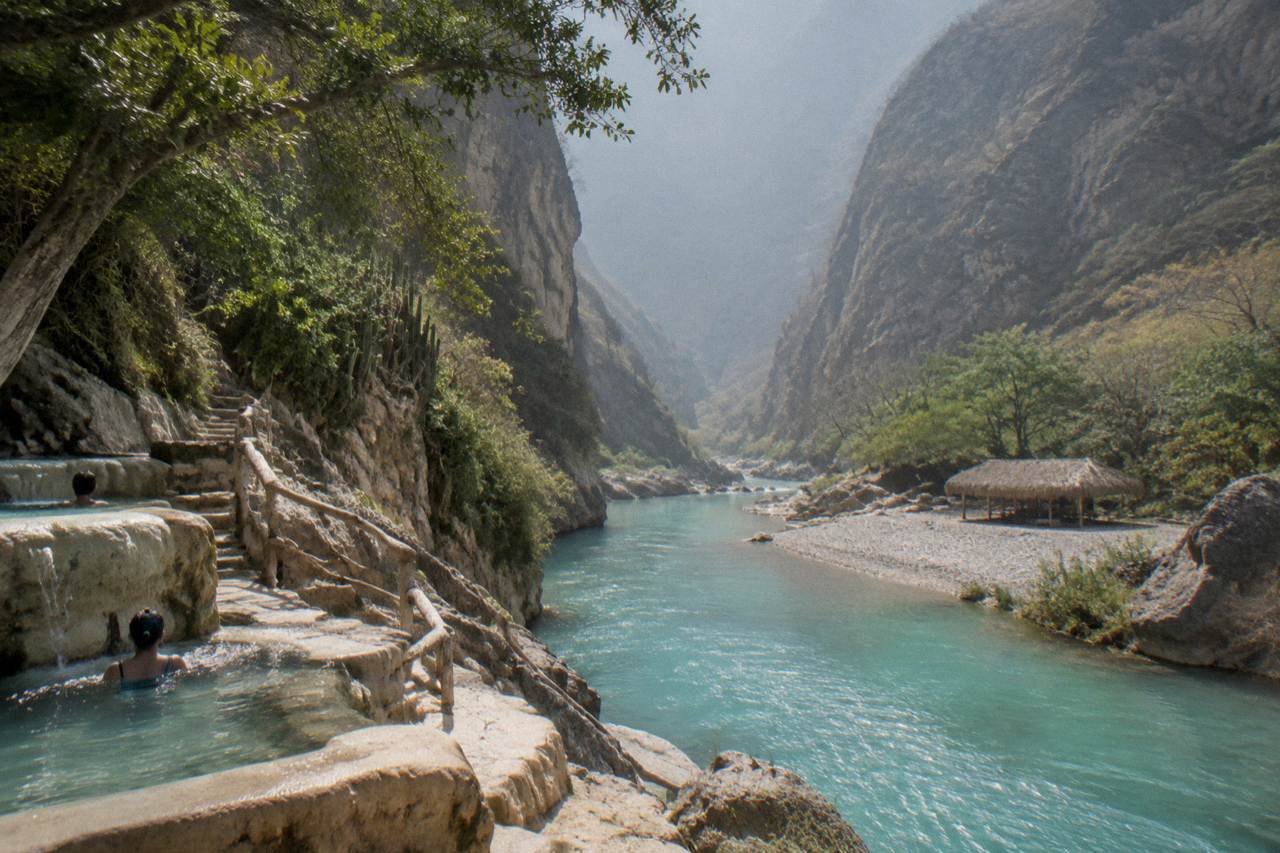 Steep canyon walls rising above the thermal river at Grutas de Tolantongo under a hazy sky