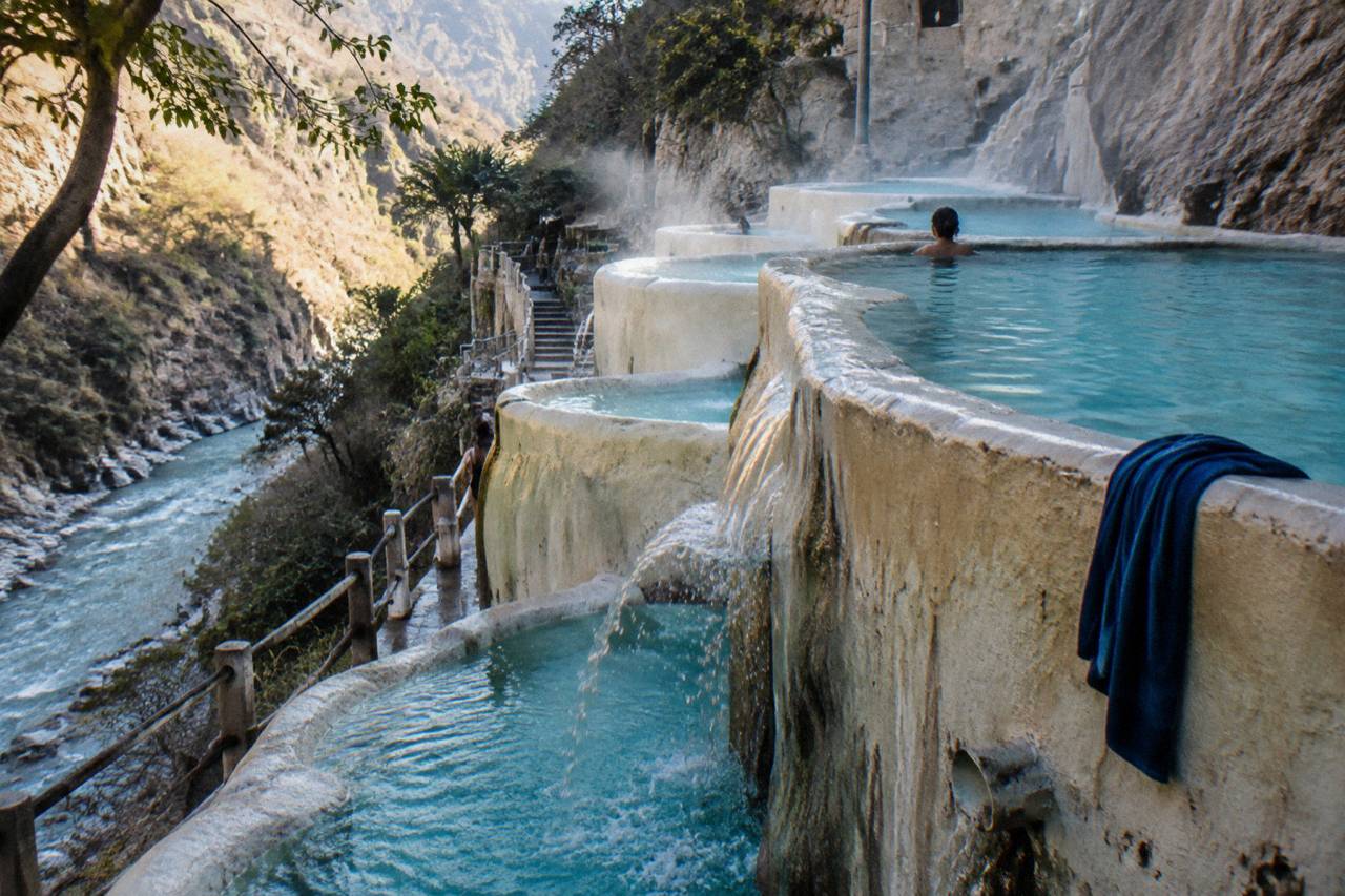 Terraced turquoise pools built along a steep canyon wall above a thermal river