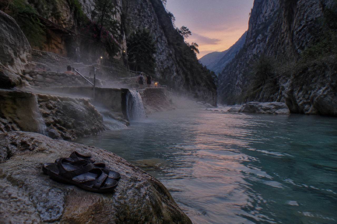 A narrow canyon with steam drifting above a thermal river at dusk
