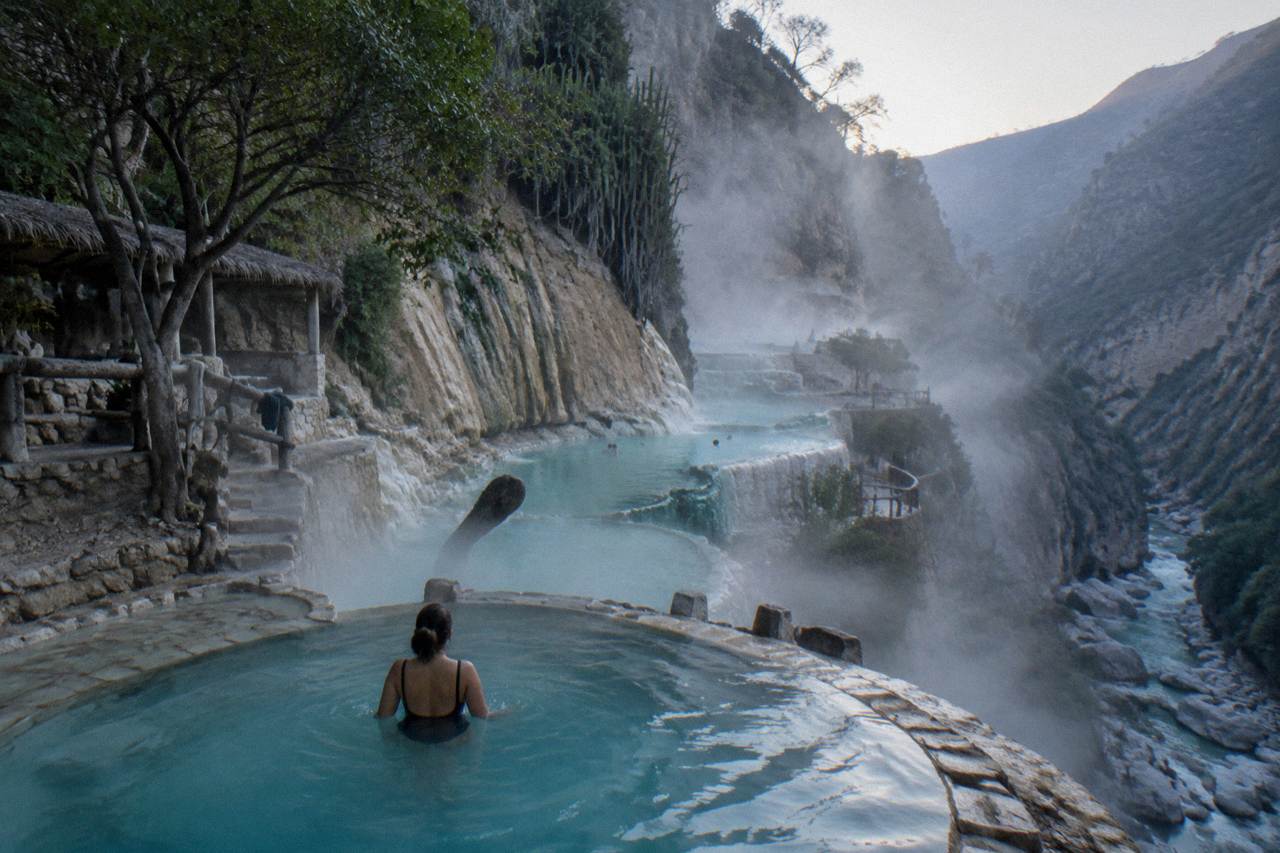 Steam rising from turquoise thermal pools built into the cliffside of a narrow canyon