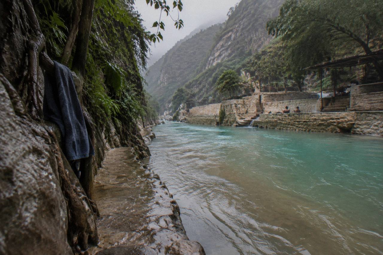 Turquoise thermal river flowing between steep canyon walls dotted with green vegetation
