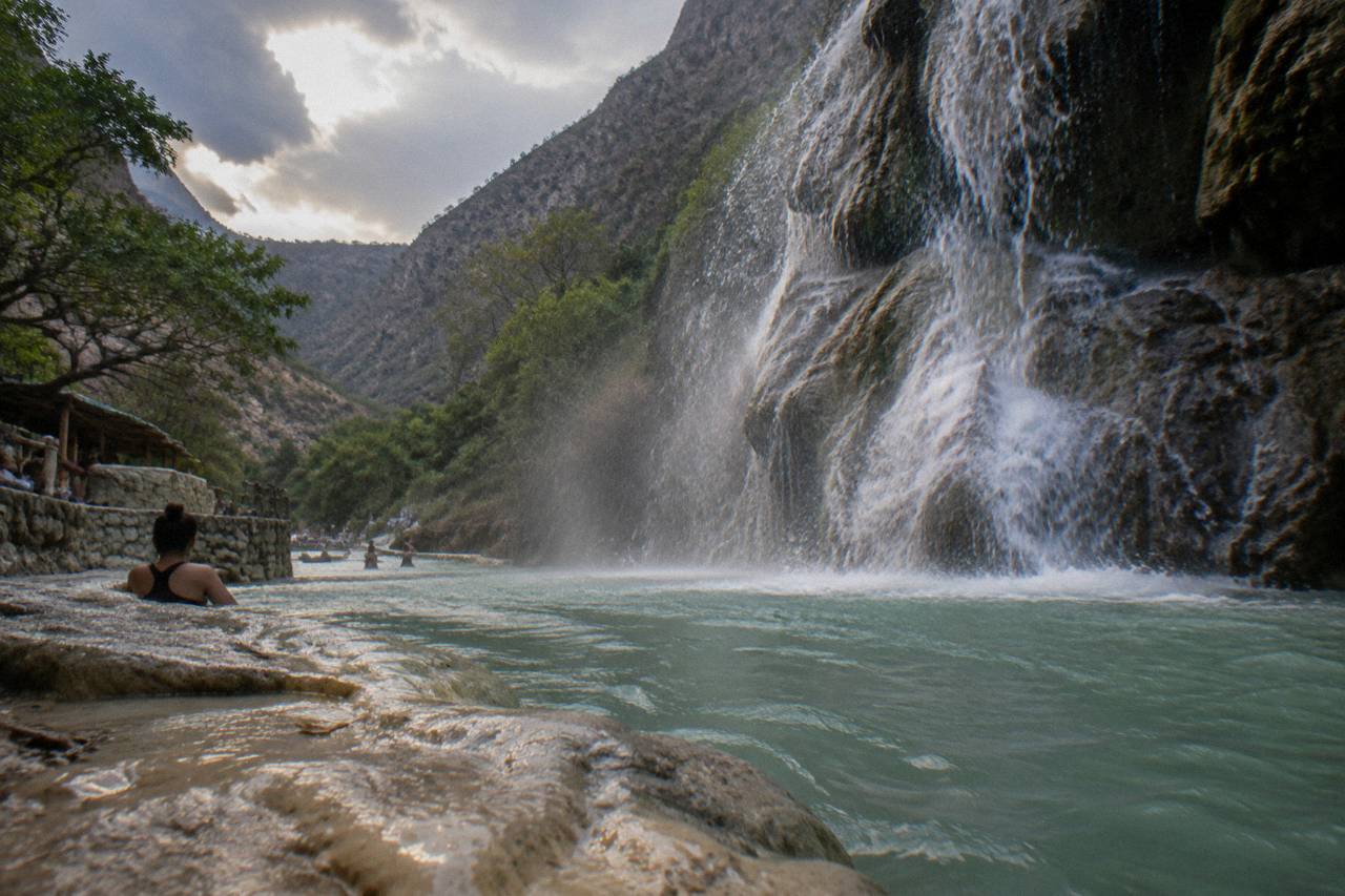 A waterfall spilling over a rock face into a green pool inside a narrow canyon