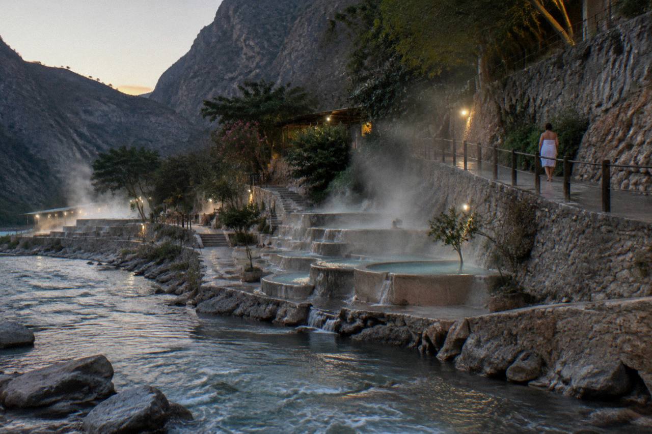 Terraced thermal pools and steam rising along a canyon riverbank