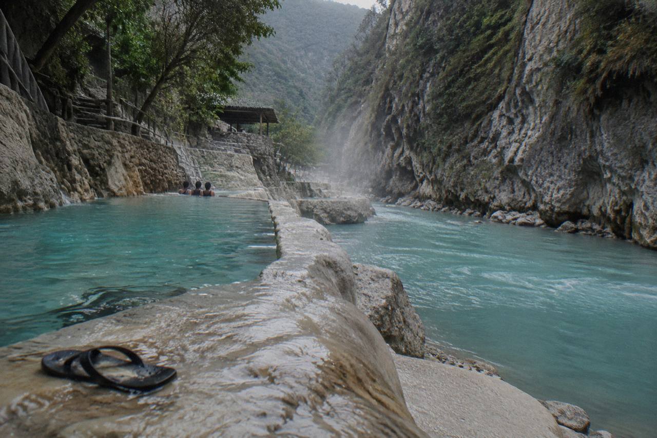 Warm turquoise river flowing between tall canyon walls with scattered pools along the bank