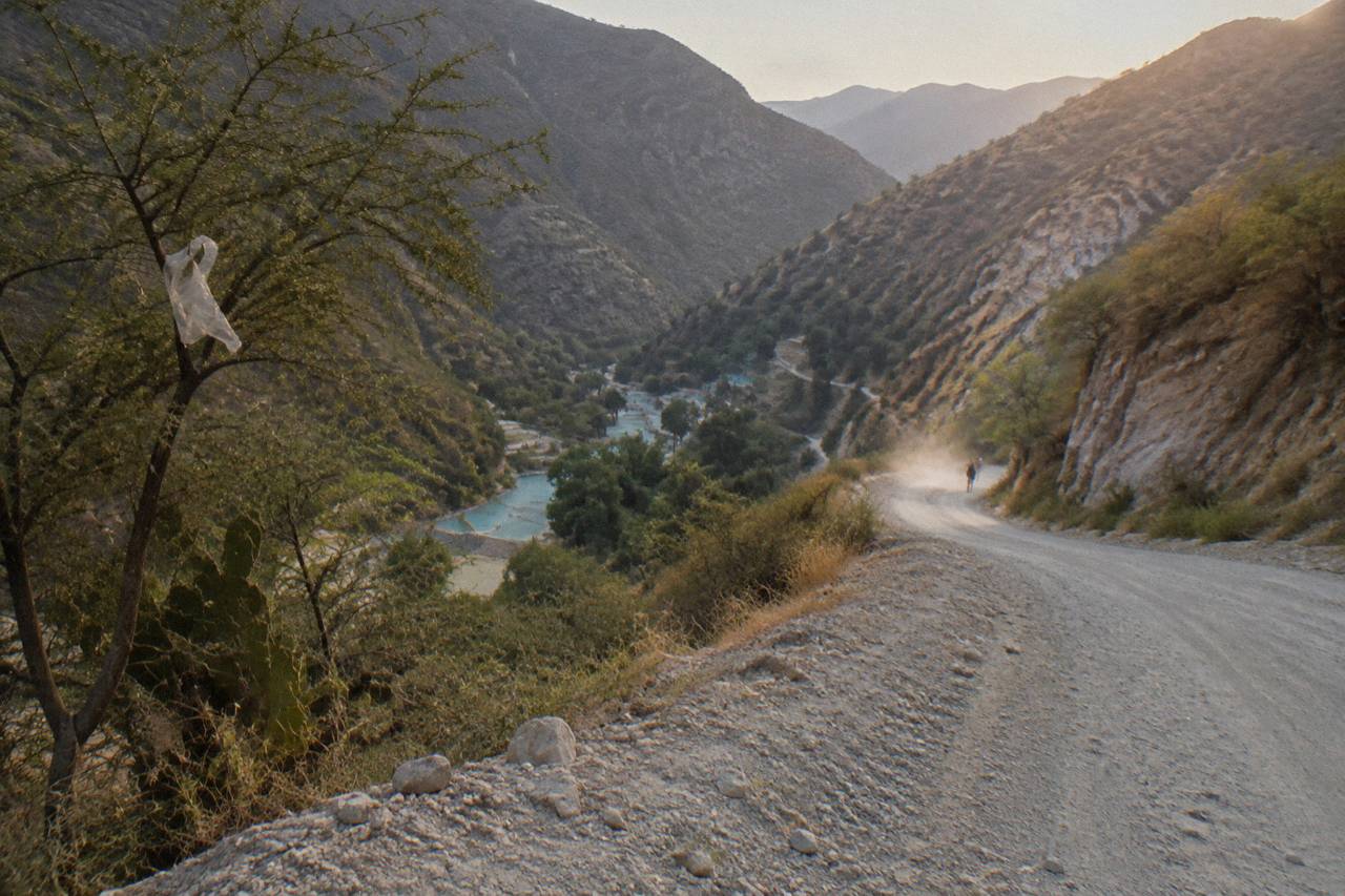 Winding mountain road descending toward a deep canyon with dry hills on both sides