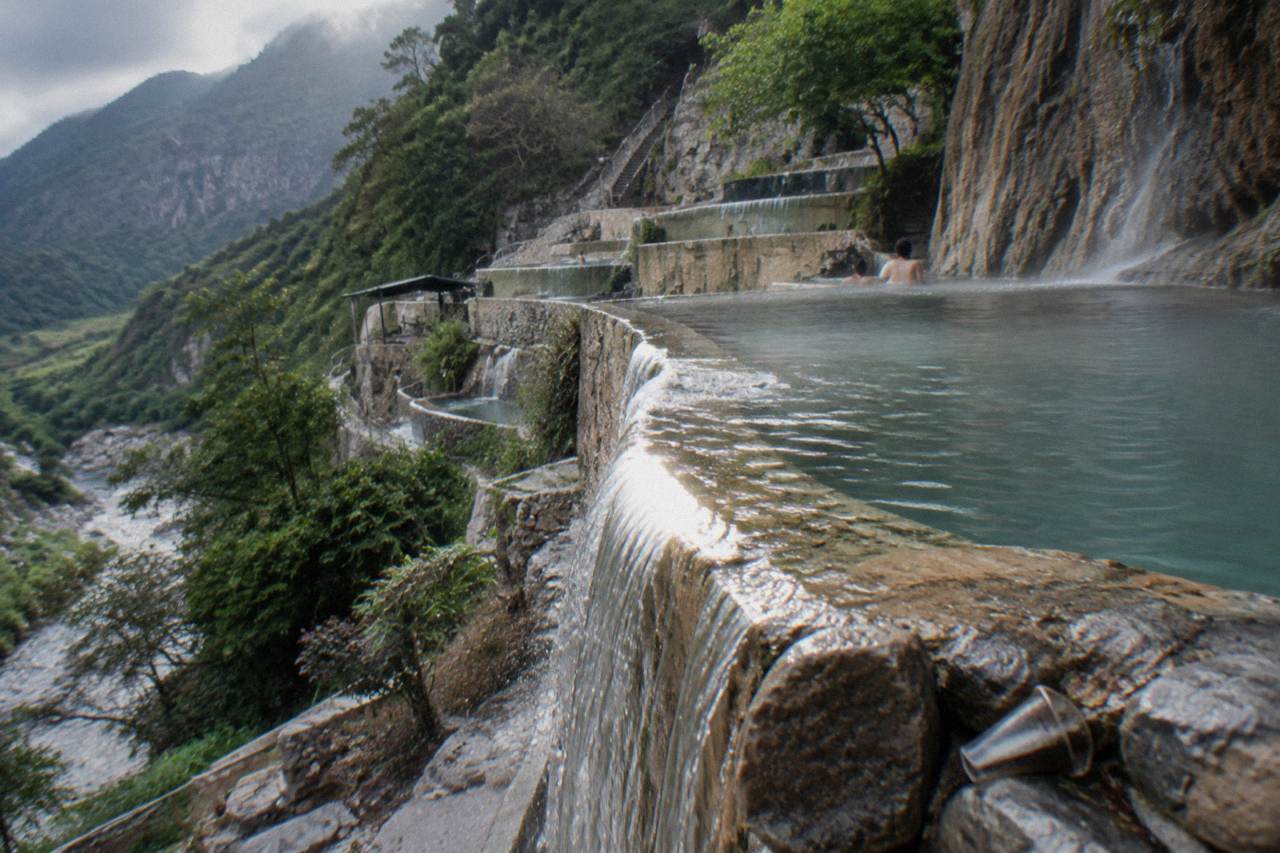 Stacked thermal pools terraced down a cliffside with steam rising over green water