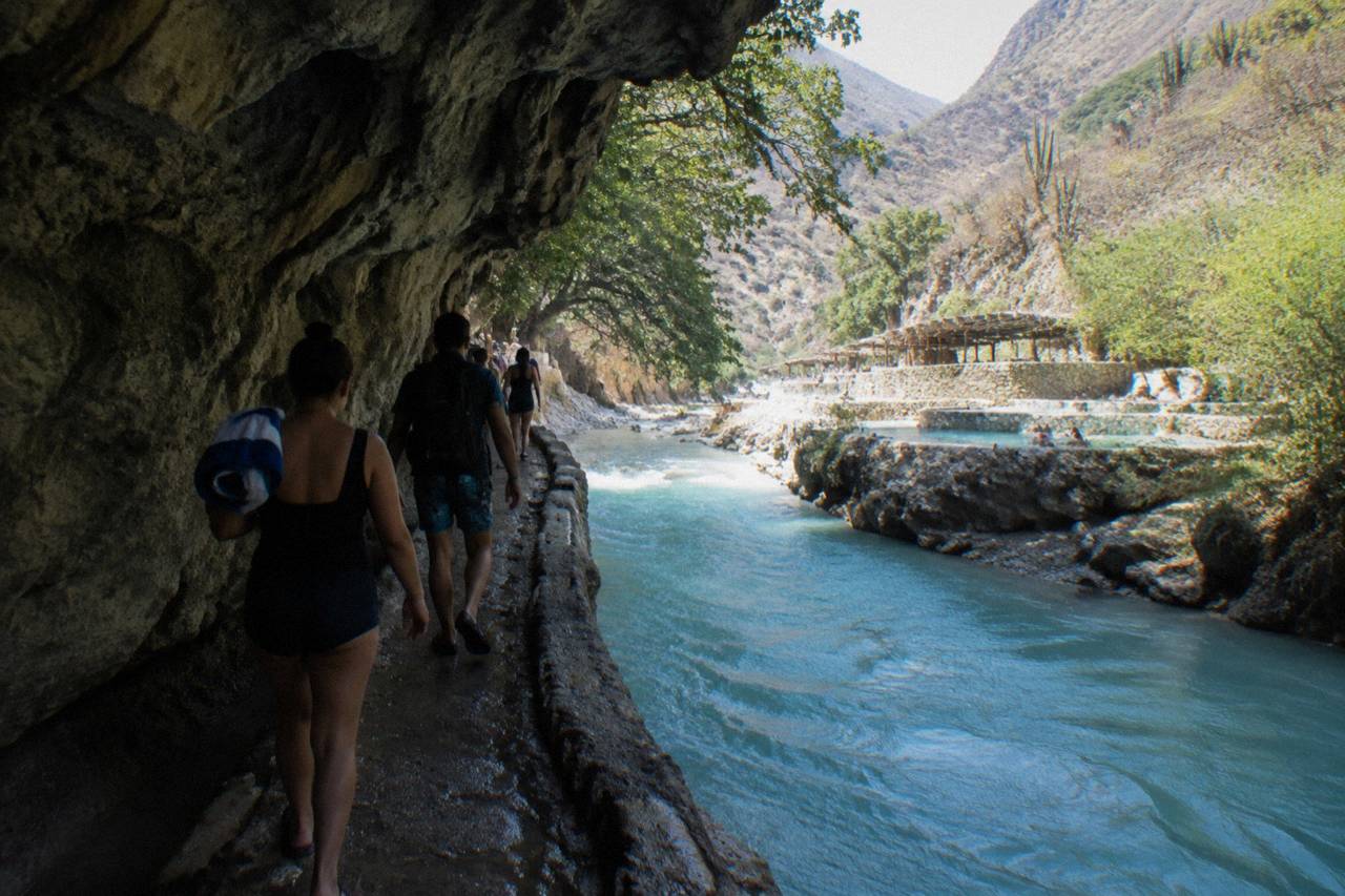 Group of visitors walking a narrow canyon path beside a warm river in the late morning
