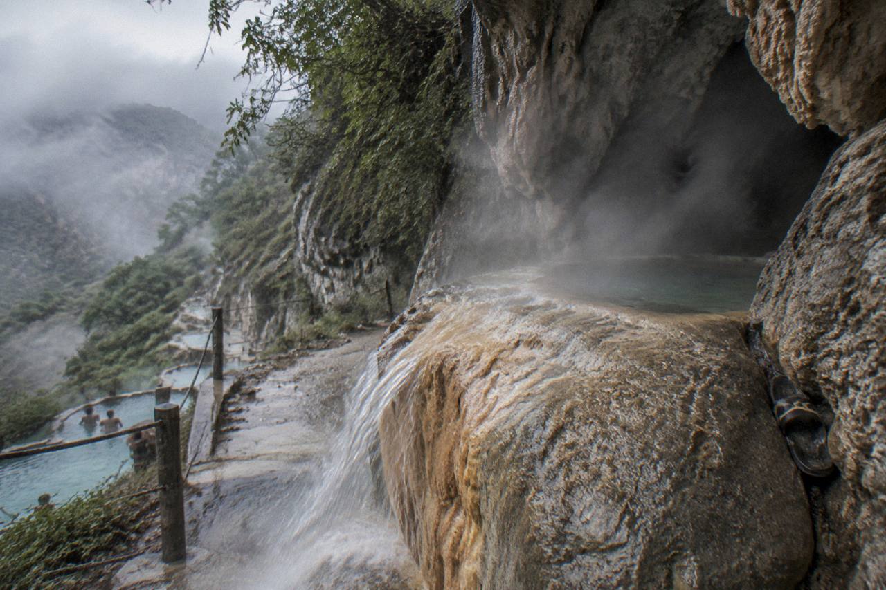 Steaming cave opening in a rock wall with warm water flowing out over smooth stone