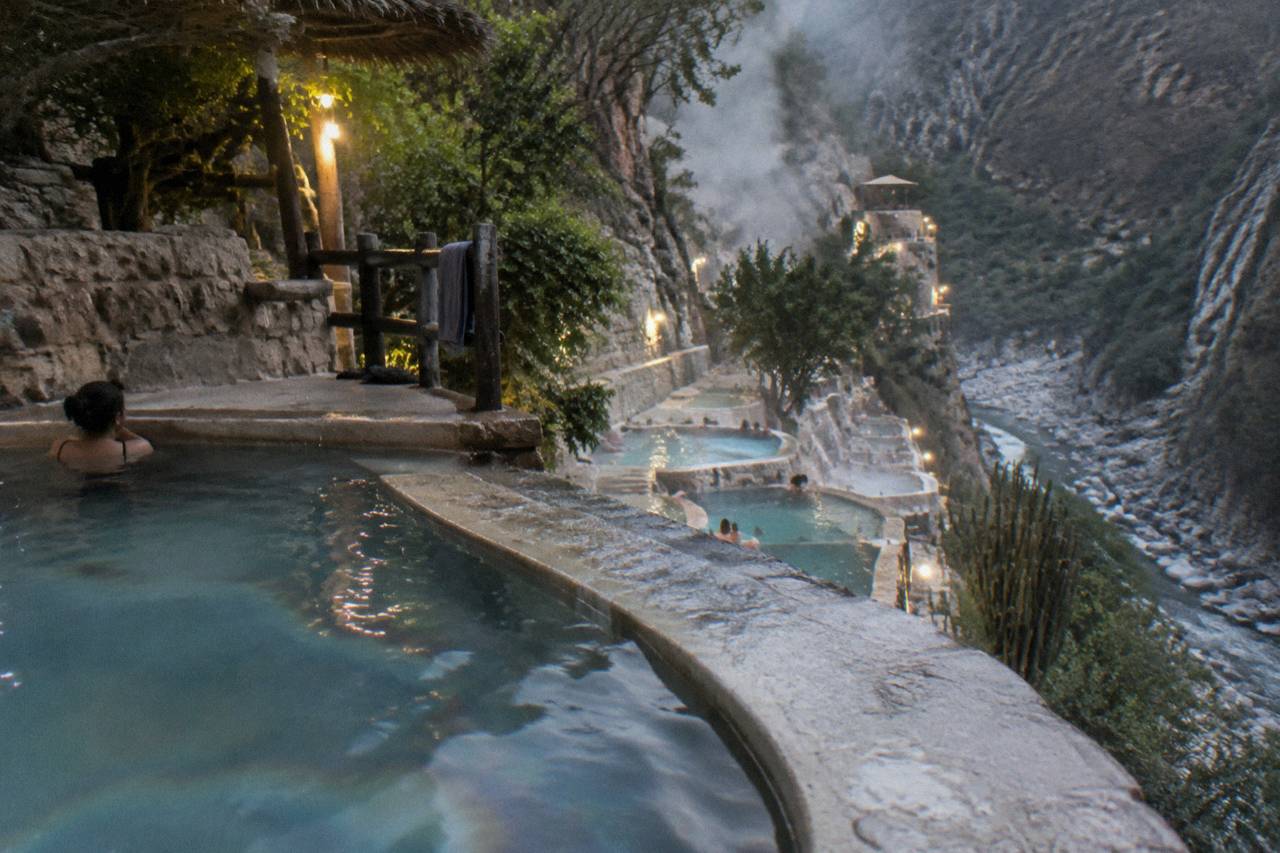 Stepped thermal pools built into the canyon wall with warm water and mountain views