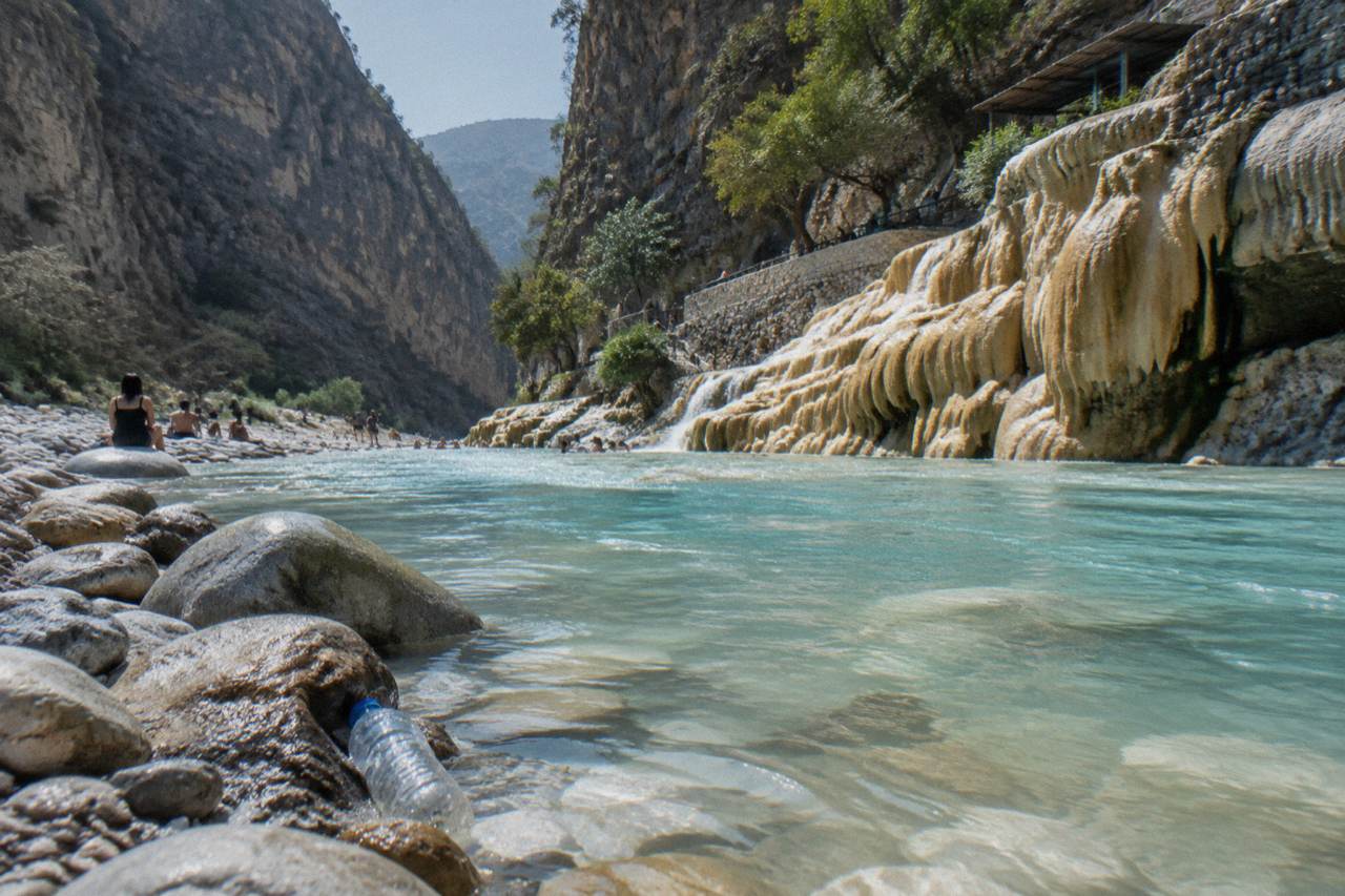 A shallow turquoise thermal river flowing between canyon walls at Tolantongo