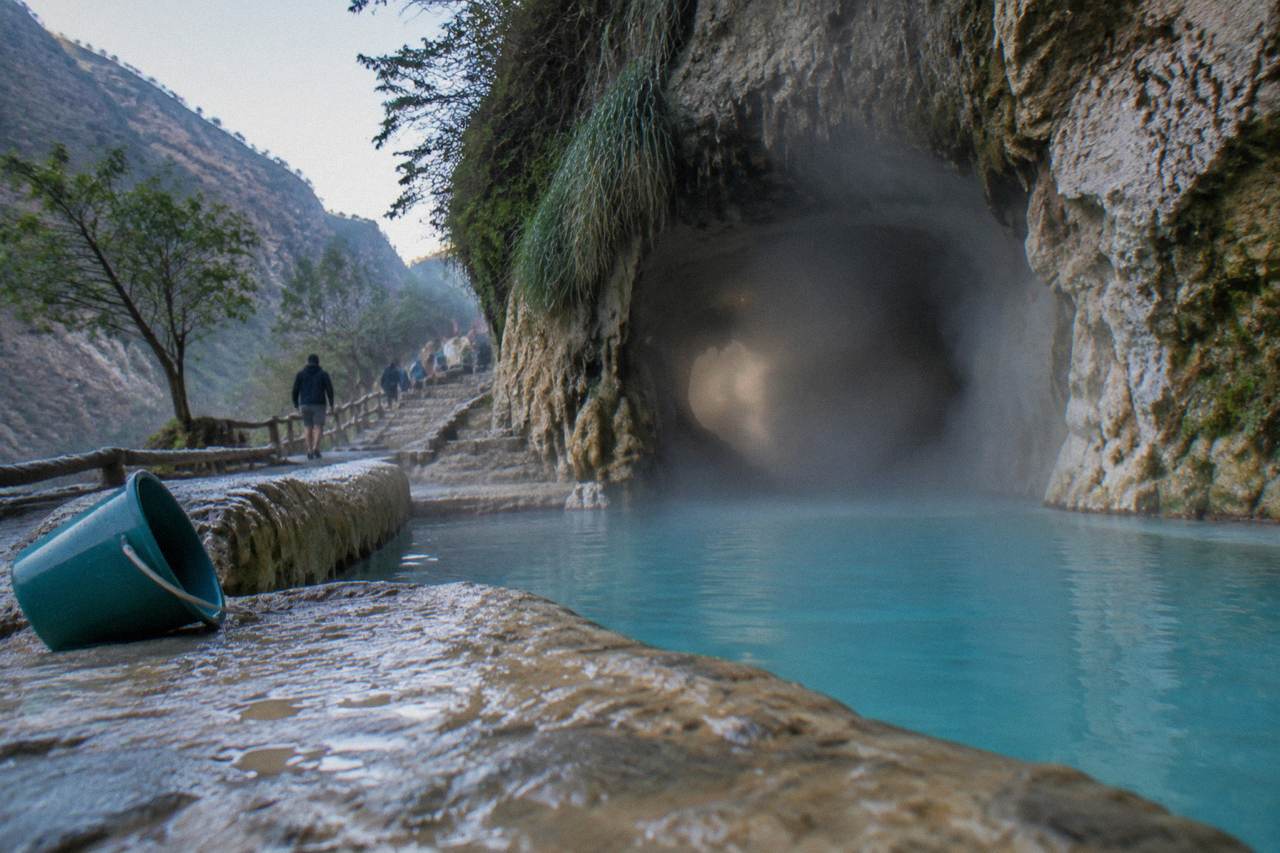 Steam drifting from the cave entrance above a turquoise pool at Tolantongo
