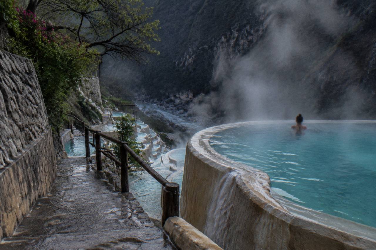 Steam rising off turquoise thermal pools cut into a canyon wall in early morning light