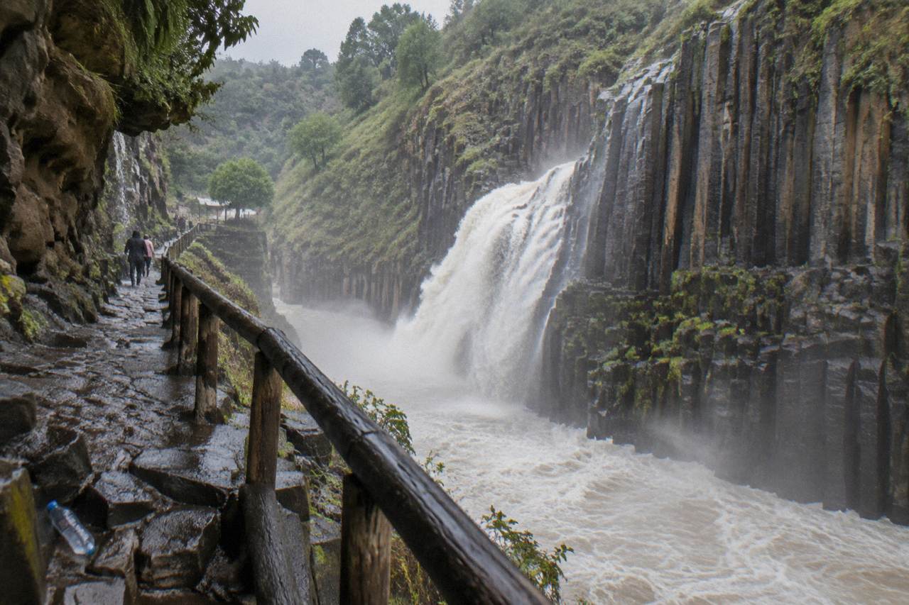 Tall vertical basalt rock columns forming a canyon wall beside falling water