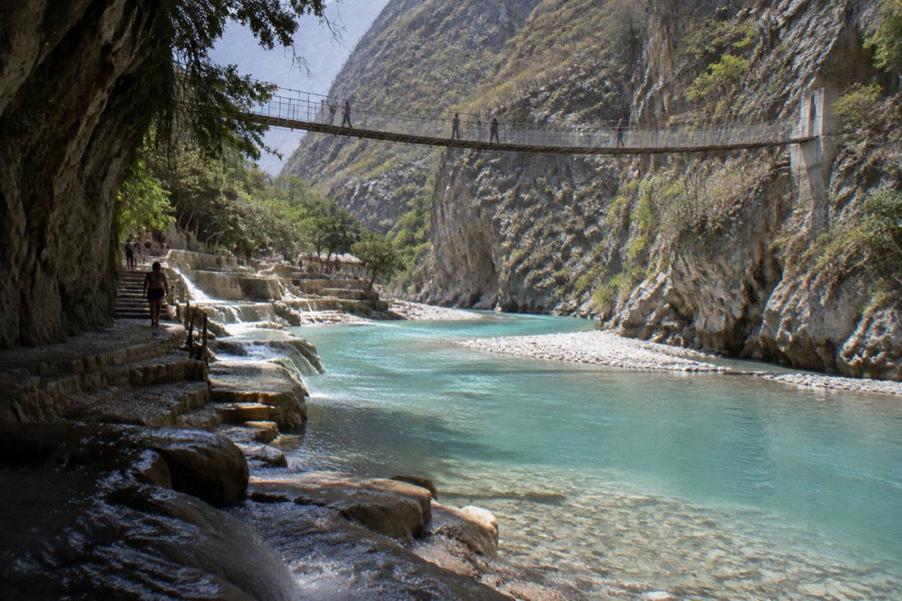 Turquoise thermal river flowing between rock walls with a suspension bridge above
