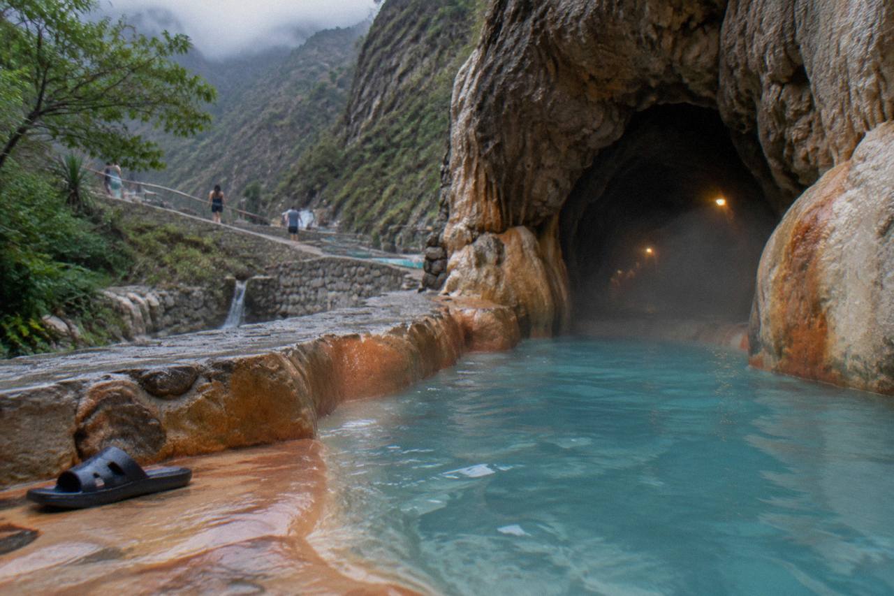 Warm blue thermal water flowing from a cave mouth into a rock channel inside a canyon