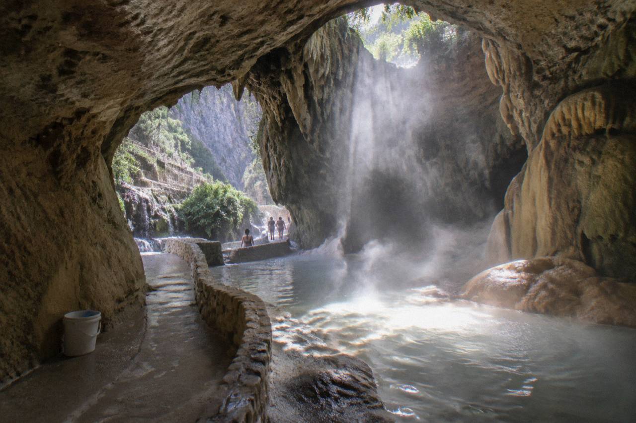Sunlight entering a steamy cavern where warm water pools on a rock floor