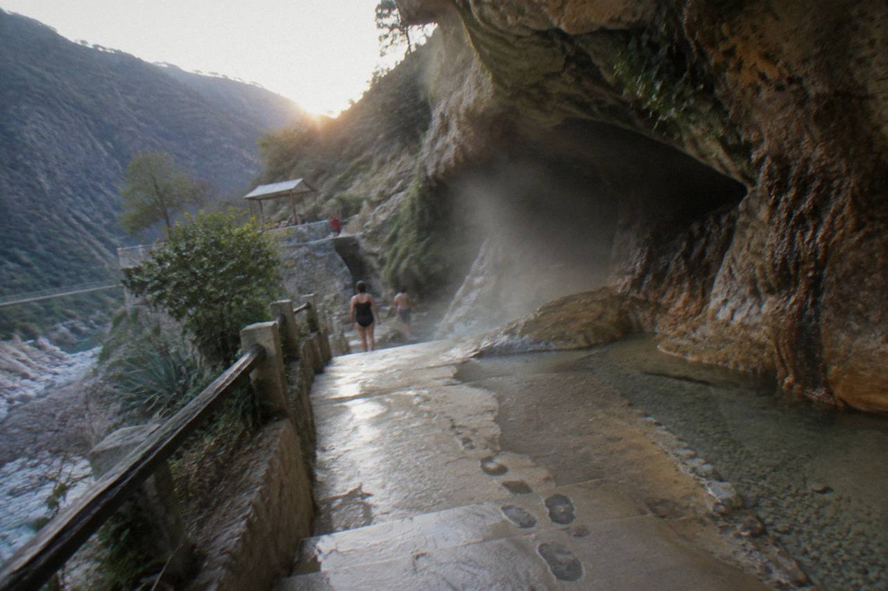 Rocks and shallow warm water at a cave entrance with mist drifting across the frame