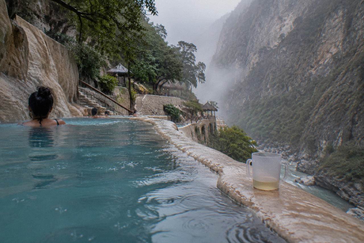 Steam rising from a thermal pool complex against a steep canyon wall