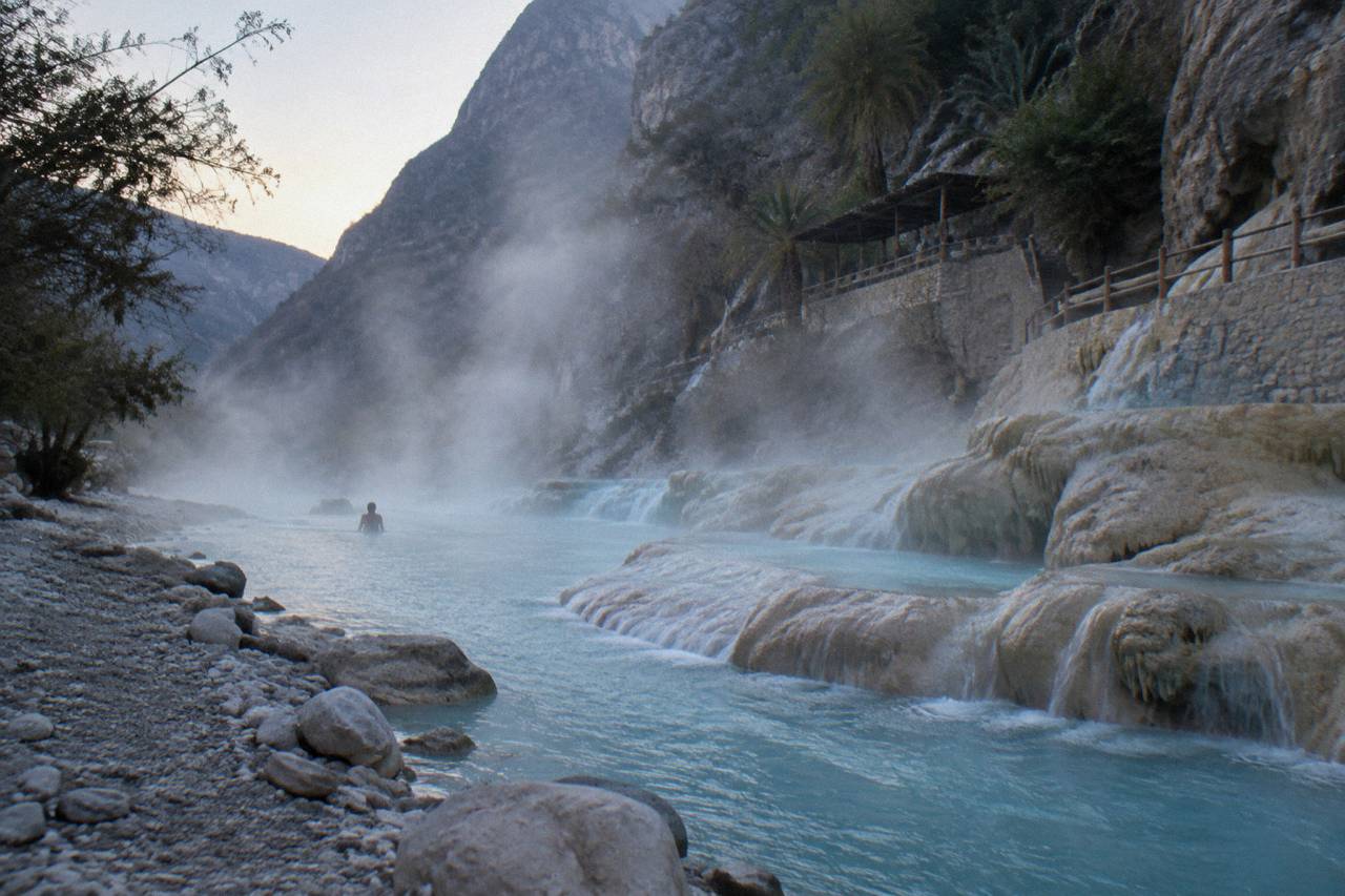 Blue thermal water flowing over rocks in the Tolantongo river with canyon walls behind