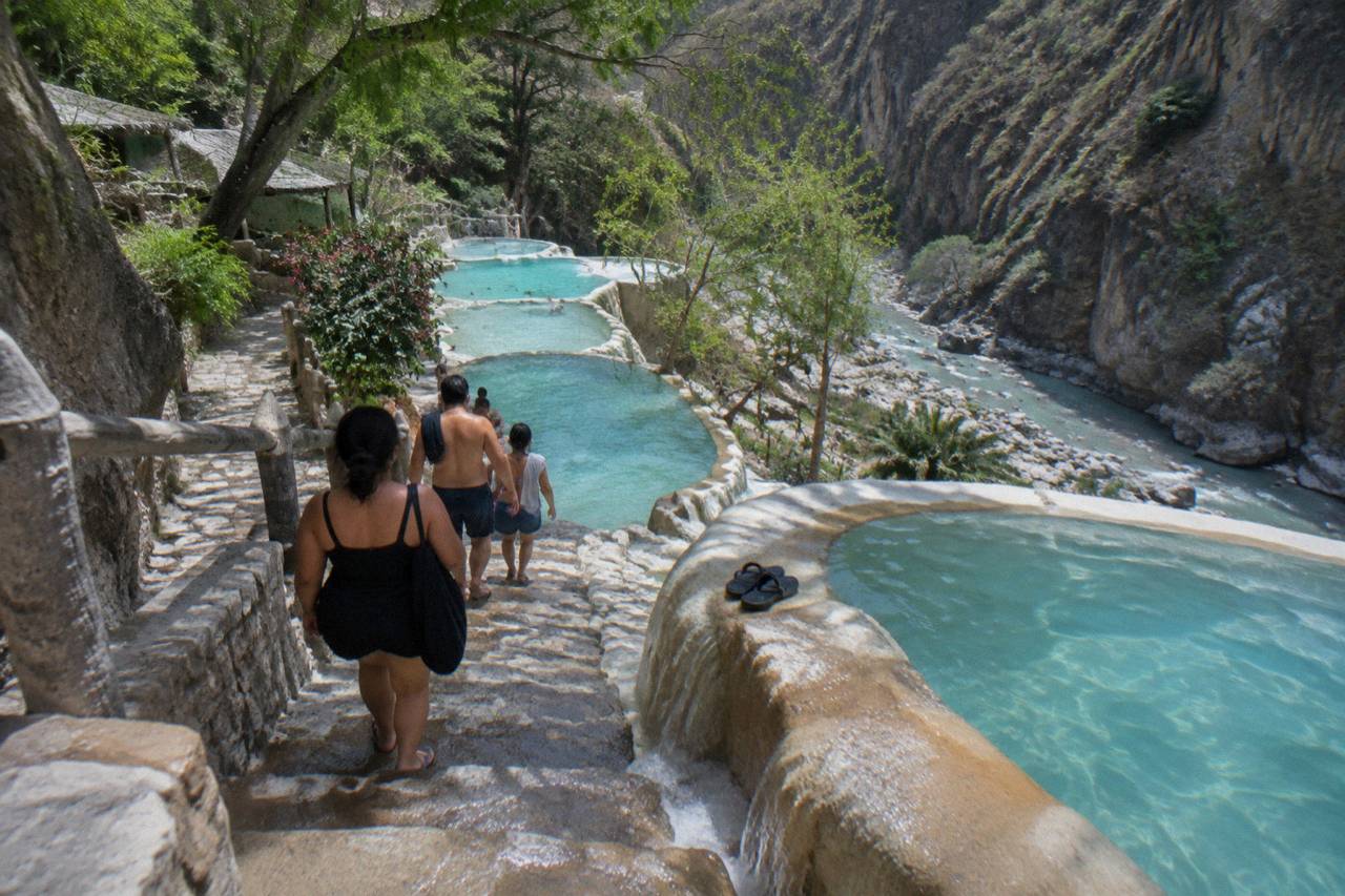 Small group of travellers walking a stone path beside turquoise thermal pools