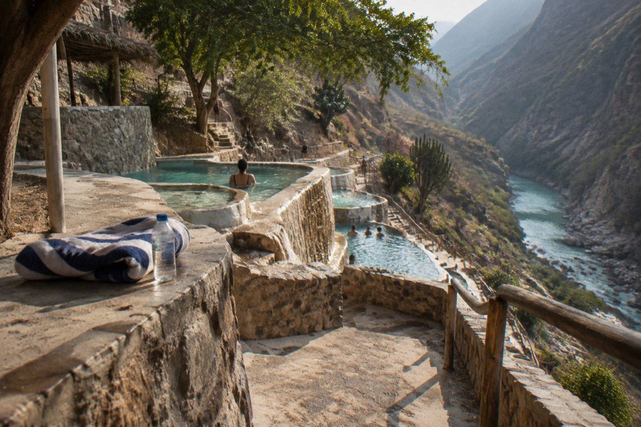 Small stone soaking pools terraced along a canyon cliff above green water