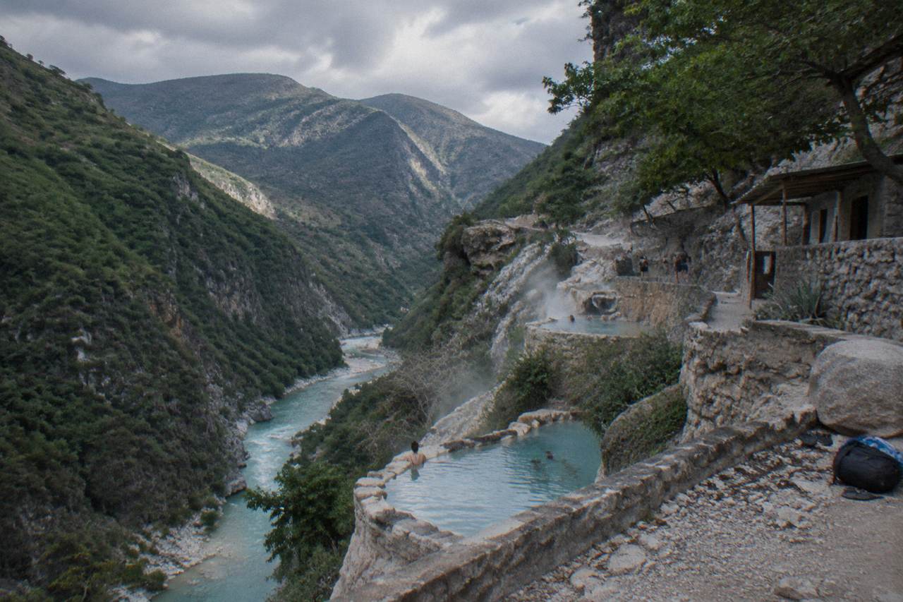 A wide canyon with a turquoise thermal river and steam rising from pools