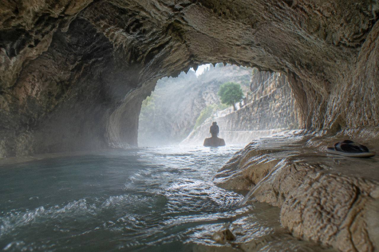 A steam-filled tunnel opening in rock leading to thermal water