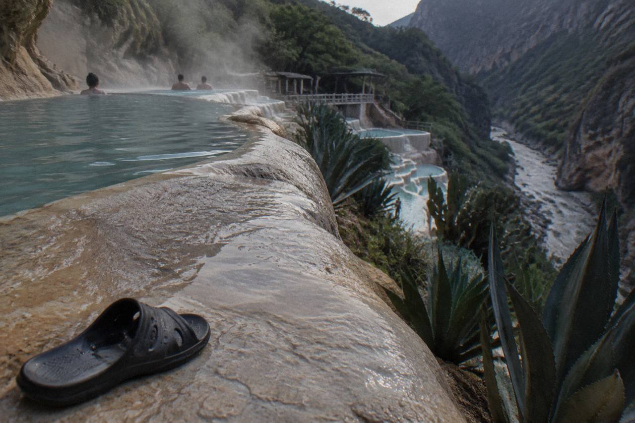 Terraced thermal pools on a green canyon slope with steam rising