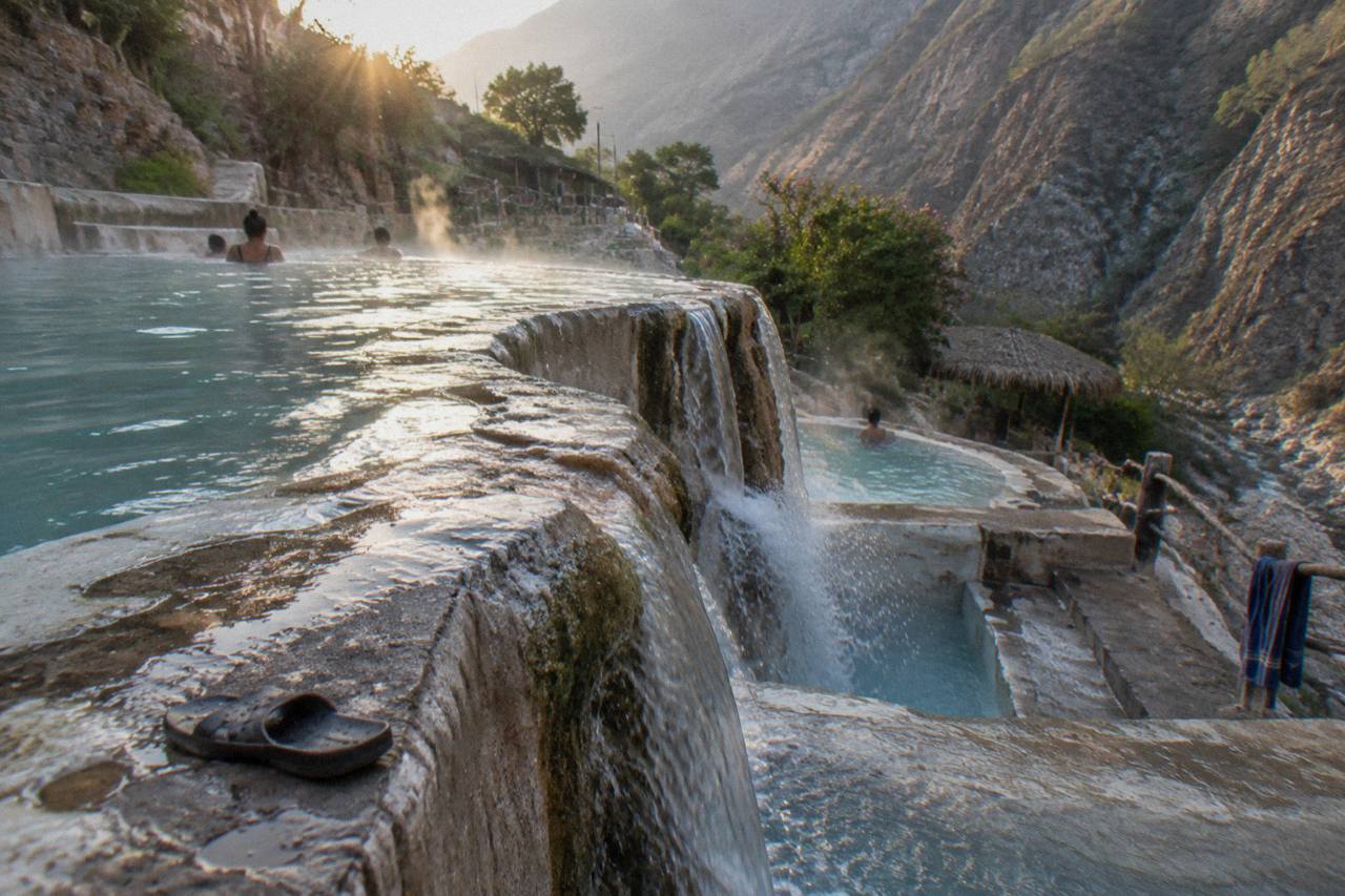 Stepped turquoise thermal pools descending a steep canyon wall with steam rising