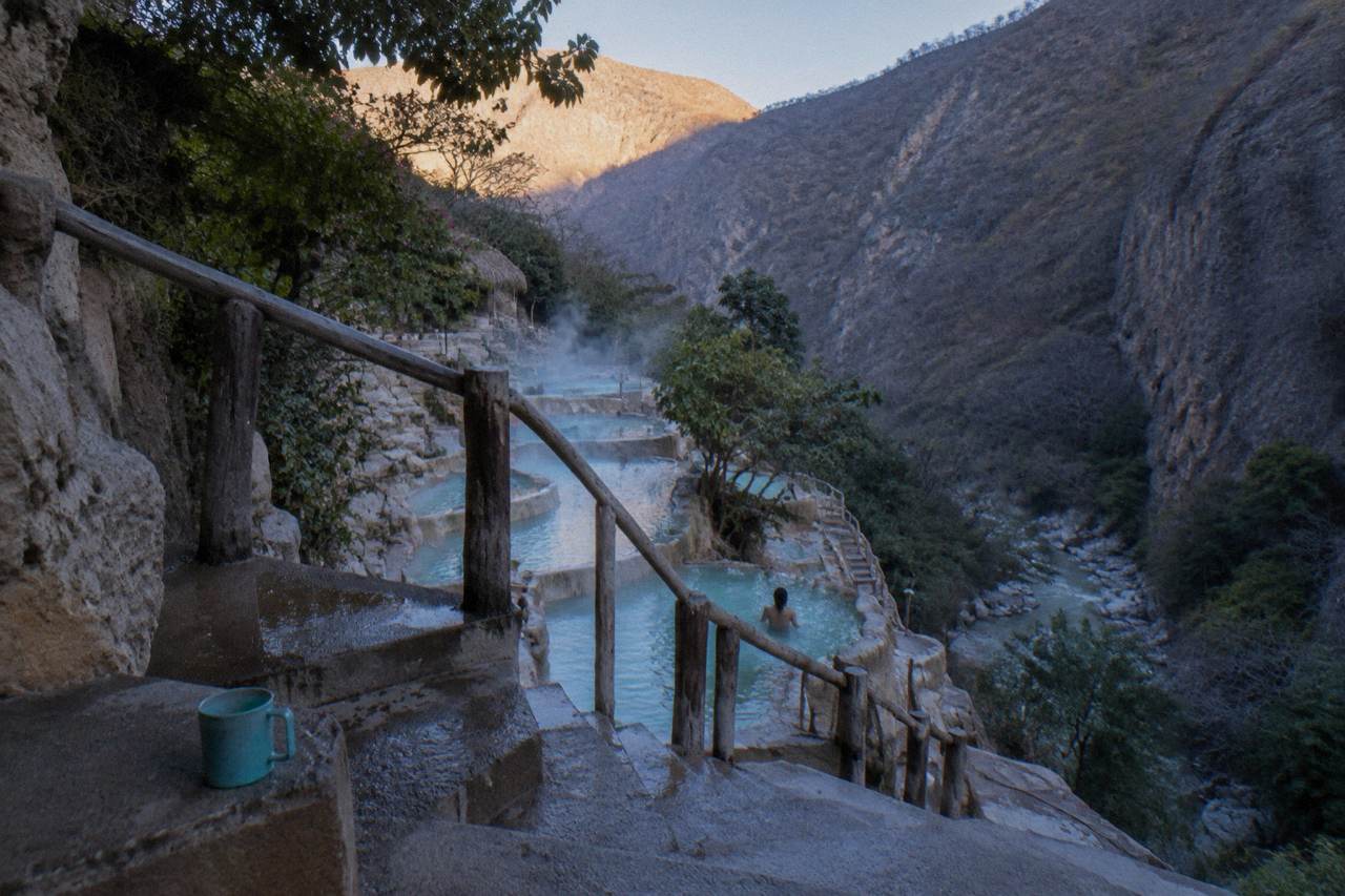 Morning sunlight reaching the top of a canyon while thermal pools below sit in soft shade